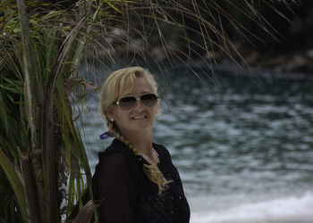 Portrait of young woman against palm tree at beach