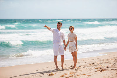 Rear view of couple standing at beach against sky