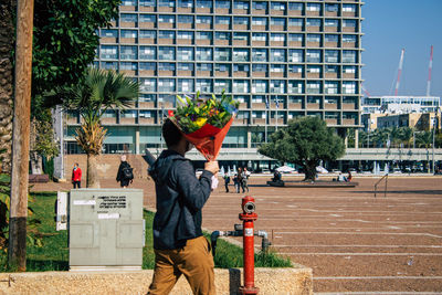 Rear view of woman standing against plants in city