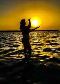 Silhouette man standing in sea against sky at sunset