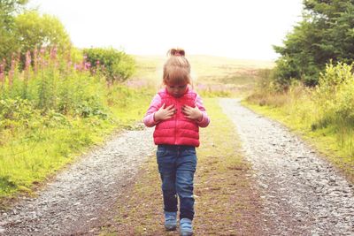 Rear view of girl walking on road amidst field