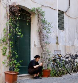 Woman sitting by potted plants against building