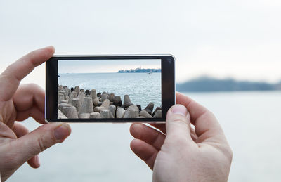 Cropped hands of man photographing sea with mobile phone