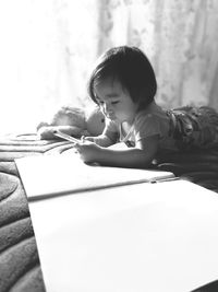 Cute girl drawing on book while lying on bed at home