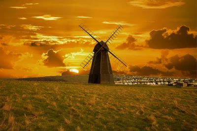 Traditional windmill on field against sky during sunset