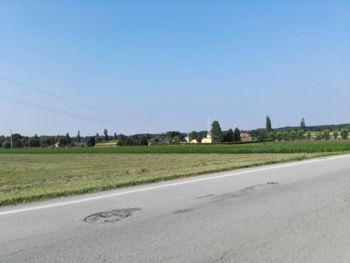 Road by field against clear blue sky