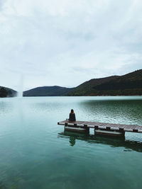 Woman sitting on lake against sky