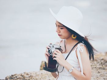 Young woman with camera standing against sky