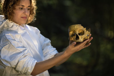 Doctor in a white anti-epidemic suit holding a decorative skull. an artificial human skullt.