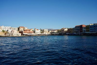 Buildings by sea against clear blue sky