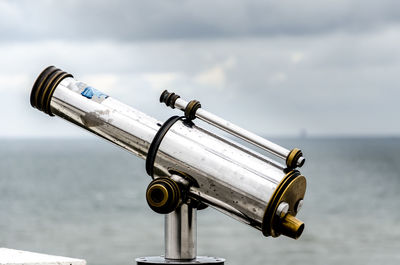 Close-up of coin-operated binoculars by sea against sky