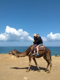 People riding camel at beach against sky