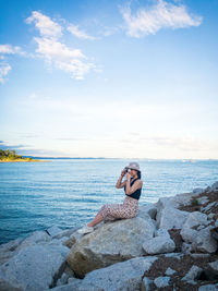 Man relaxing on rock by sea against sky