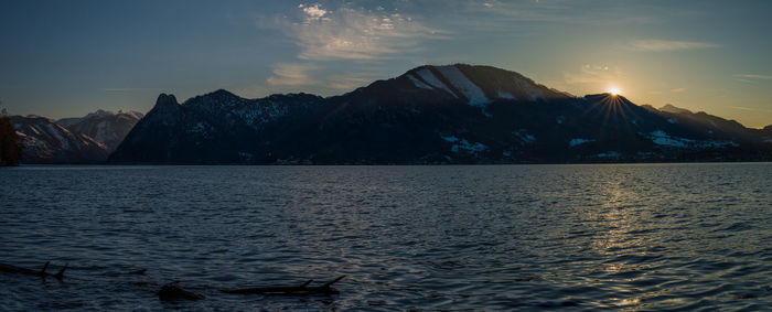 Scenic view of sea by mountains against sky during sunset