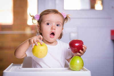Cute baby girl with fruits on high chair at home