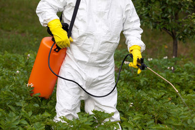 Midsection of farmer spraying pesticide on plants