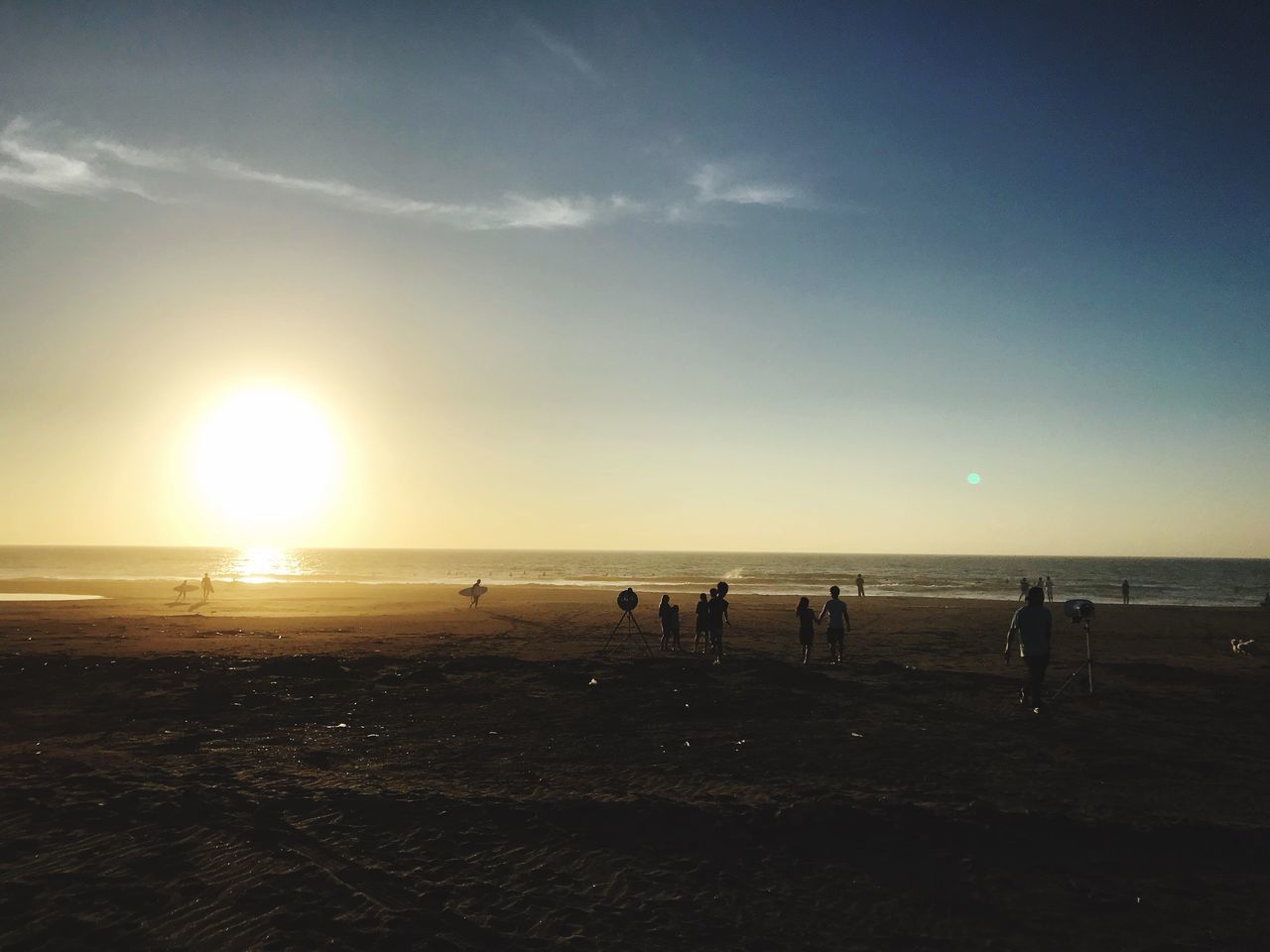 sky, land, group of people, water, beach, sun, sea, sunlight, horizon, beauty in nature, silhouette, scenics - nature, real people, nature, crowd, sunset, leisure activity, large group of people, horizon over water, outdoors, lens flare