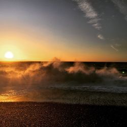 Scenic view of waves splashing in sea against sky at sunset