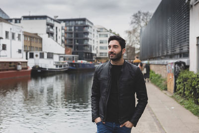 Man looking away while standing by canal in city