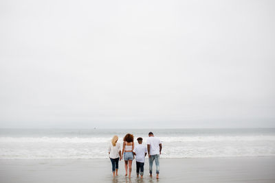 Rear view of people at beach against sky