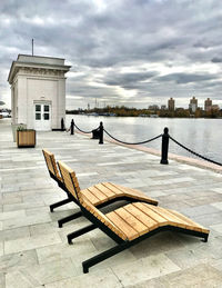 Bench on pier by lake against sky