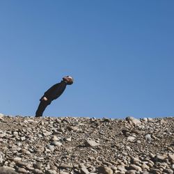 Low angle view of man jumping on rocks against clear blue sky