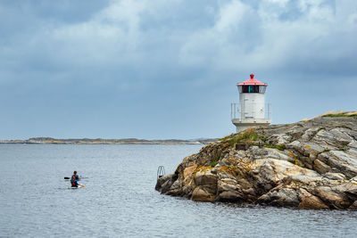 Lighthouse on rock by sea against sky