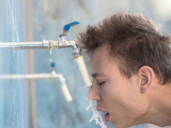 Side view of man drinking water from faucet