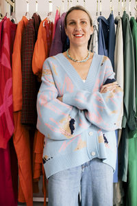 Portrait of female owner with arms crossed standing against clothes in boutique