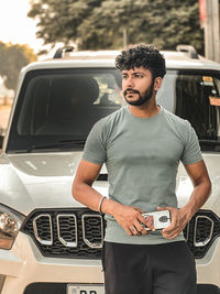 Side view of young man standing alone near car