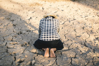 Rear view of person kneeling on cracked field