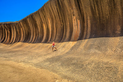 Woman standing with arms outstretched by cliff