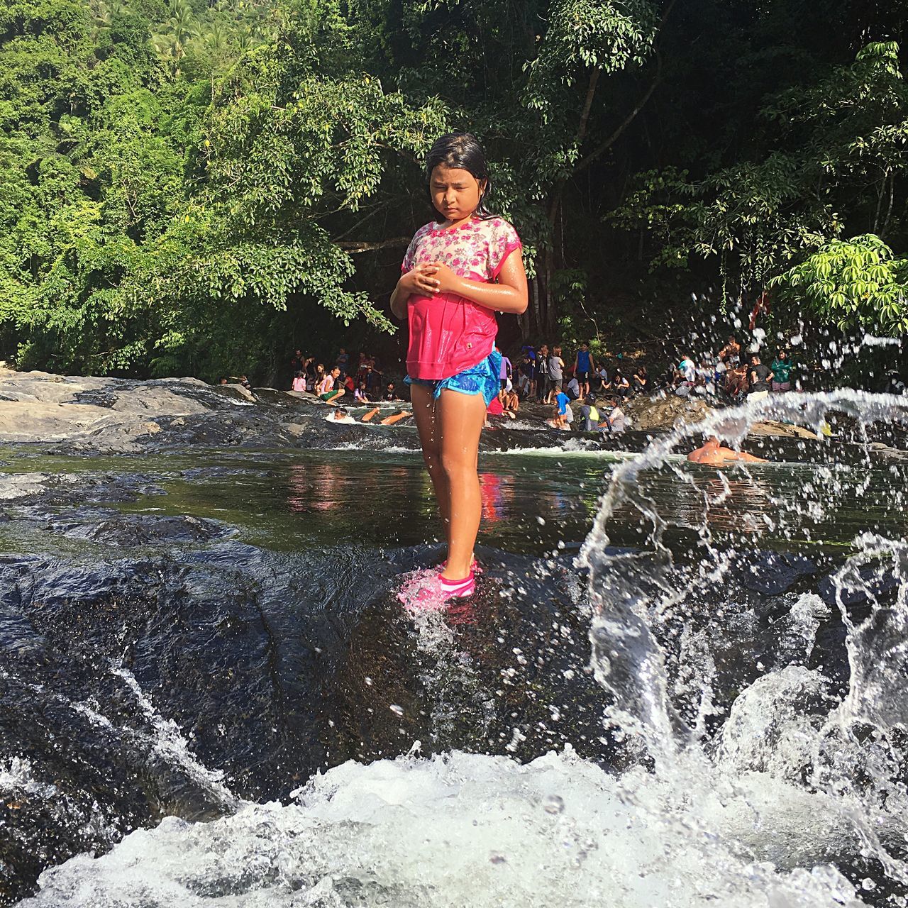 water, fun, real people, leisure activity, one person, front view, childhood, full length, portrait, looking at camera, enjoyment, teenager, day, tree, smiling, outdoors, happiness, standing, lifestyles, nature, girls, ankle deep in water, young adult, young women, people