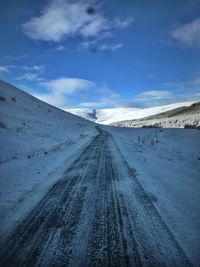 Road on snow covered landscape against sky