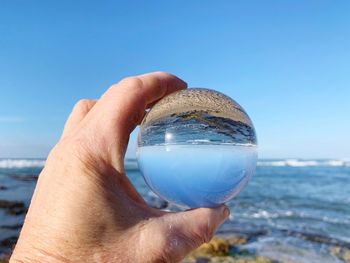 Midsection of person holding sea against clear blue sky