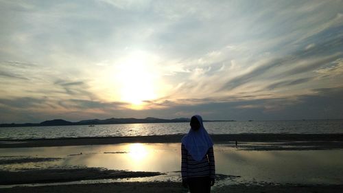 Rear view of woman looking at sea against sunset sky