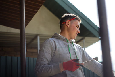 Portrait of young construction worker or architect with red pencil and glowes near house. caucasian