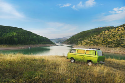 Travel trailer parked on grassy riverbank against blue sky