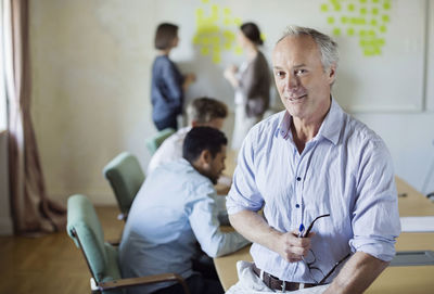 Portrait of confident businessman sitting on conference table with colleagues discussing in background