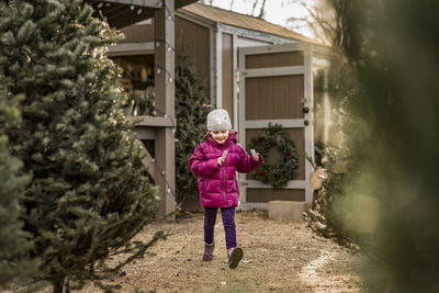 Cheerful girl holding candy canes walking by christmas trees at yard