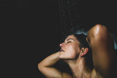 Woman under water drops. showering, black background.