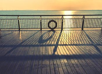 Shadow of railing on pier by sea against sky during sunset