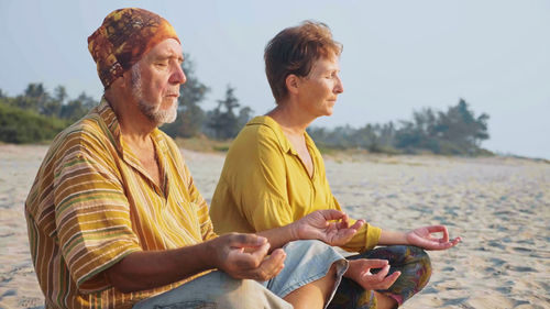 Young men sitting on land against sky