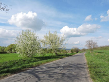 Empty road amidst field against sky