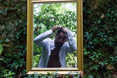 Young man adjusting hair reflecting on mirror at forest