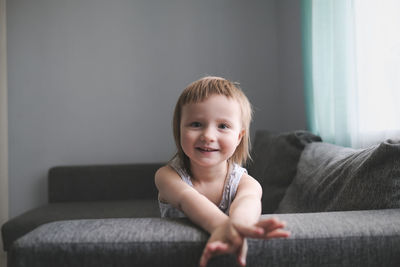 Child jumps and plays on sofa in minimalist living room, gray sofa.