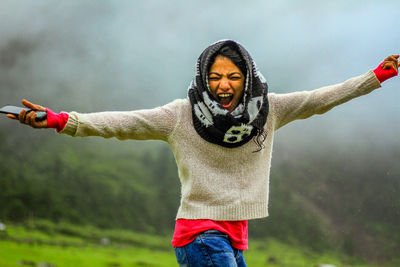 Portrait of cheerful woman with arms outstretched standing outdoors during foggy weather