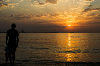 Rear view of silhouette man standing on beach during sunset