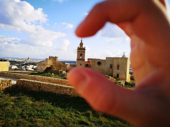 Cropped image of person holding building against sky