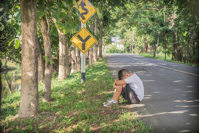 Side view of boy sitting by road